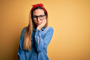 Young beautiful blonde woman with blue eyes wearing denim shirt over yellow background thinking looking tired and bored with depression problems with crossed arms.