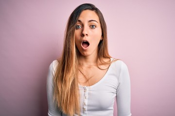 Young beautiful blonde woman with blue eyes wearing white t-shirt over pink background afraid and shocked with surprise and amazed expression, fear and excited face.