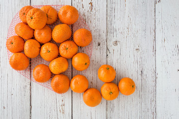 Small clementine oranges spilling from a red mesh bag onto a whitewashed wood background
