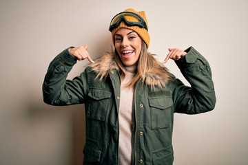 Young brunette skier woman wearing snow clothes and ski goggles over white background looking confident with smile on face, pointing oneself with fingers proud and happy.
