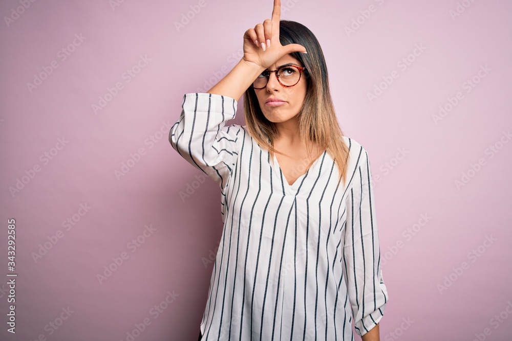 Sticker young beautiful woman wearing casual striped t-shirt and glasses over pink background making fun of 