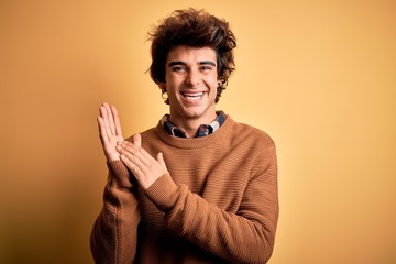 Young handsome man wearing casual shirt and sweater over isolated yellow background clapping and applauding happy and joyful, smiling proud hands together