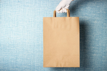 A woman's hand in white glove holds cardboard bag, against a blue background