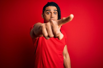 Young handsome african american afro man with dreadlocks wearing red casual t-shirt Pointing with finger surprised ahead, open mouth amazed expression, something on the front