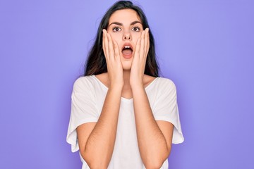 Young beautiful brunette woman wearing casual white t-shirt over purple background afraid and shocked, surprise and amazed expression with hands on face