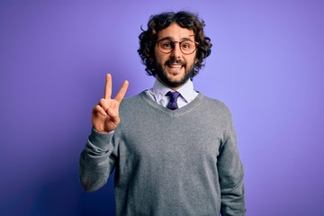 Handsome businessman with beard wearing tie and glasses standing over purple background smiling with happy face winking at the camera doing victory sign. Number two.