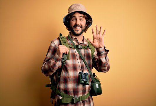 Young hiker man with curly hair and beard hiking wearing backpack and water canteen Waiving saying hello happy and smiling, friendly welcome gesture