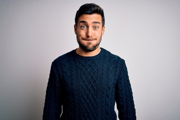 Obraz premium Young handsome man with beard wearing casual sweater standing over white background puffing cheeks with funny face. Mouth inflated with air, crazy expression.