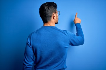 Young handsome man with beard wearing casual sweater and glasses over blue background Posing...