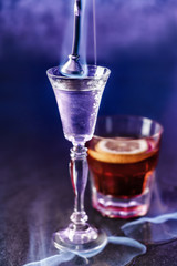 Classic alcoholic cocktails in shot glasses or shooters on dark blue background. Studio shot of drink in freeze motion, burning cocktail, stylized