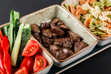 Sport nutrition with pasta, fried liver and fresh vegetables in plate on black background. Healthy food, dieting, top view