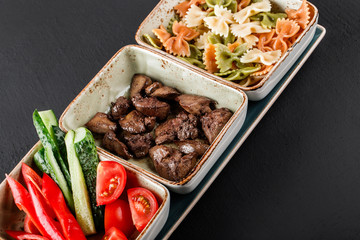 Sport nutrition with pasta, fried liver and fresh vegetables in plate on black background. Healthy food, dieting, top view