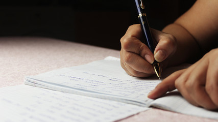 
Woman writes with pen on paper at the table