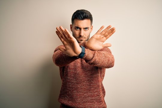 Young handsome man wearing casual sweater standing over isolated white background Rejection expression crossing arms and palms doing negative sign, angry face