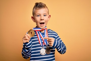 Young little caucasian winner kid wearing award competition medals over yellow background very...