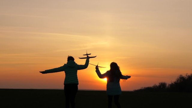 Silhouette of healthy children playing on an airplane. Dreams of flying. concept of happy childhood. Two free girls play with toy airplane. Children on background of sun with an airplane in his hand.