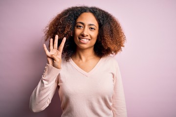 Young african american woman with afro hair wearing casual sweater over pink background showing and pointing up with fingers number four while smiling confident and happy.