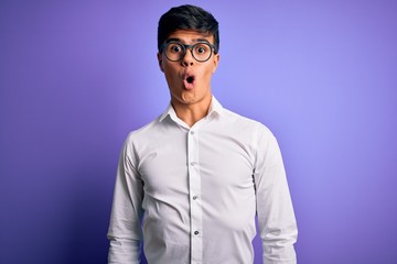 Young handsome business man wearing shirt and glasses over isolated purple background afraid and shocked with surprise expression, fear and excited face.