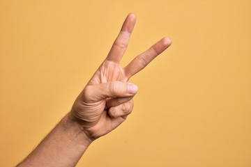Hand of caucasian young man showing fingers over isolated yellow background counting number 2 showing two fingers, gesturing victory and winner symbol - obrazy, fototapety, plakaty