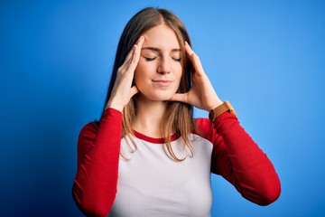 Young beautiful redhead woman wearing casual t-shirt over isolated blue background with hand on head for pain in head because stress. Suffering migraine.