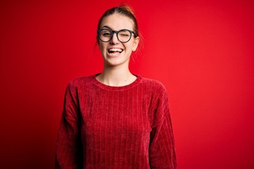 Young beautiful redhead woman wearing casual sweater over isolated red background winking looking at the camera with sexy expression, cheerful and happy face.