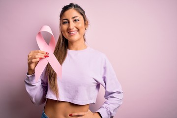 Young beautiful brunette woman holding pink cancer ribbon symbol over isolated background with a...