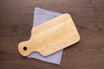 Top view above of Wooden chopping board with napkin on dark table background. Wood Cutting board with handle and hole for hanging. Empty utensil with copy space.