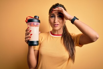 Young beautiful brunette woman holding gym bottle shaker with protein beverage for diet stressed...