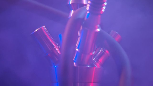 Close up of hookah metal parts in the dark room under the red and blue lights with smoke on the background. Action. Concept of traditional Turkish relaxation.
