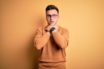 Fototapeta premium Young handsome caucasian man wearing glasses and casual winter sweater over yellow background shouting and suffocate because painful strangle. Health problem. Asphyxiate and suicide concept.