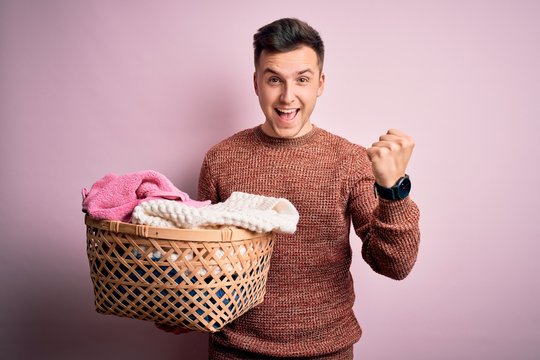 Young Handsome Caucasian Man Doing Housework Chores Holding Laundry Wicker Basket Screaming Proud And Celebrating Victory And Success Very Excited, Cheering Emotion