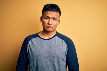 Young handsome latin man wearing casual t-shirt standing over yellow background depressed and worry for distress, crying angry and afraid. Sad expression.