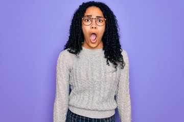 Young african american woman wearing casual sweater and glasses over purple background afraid and shocked with surprise and amazed expression, fear and excited face.