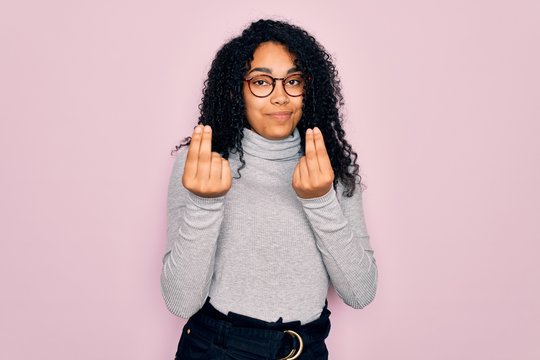 Young african american woman wearing turtleneck sweater and glasses over pink background doing money gesture with hands, asking for salary payment, millionaire business