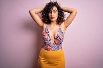 Young beautiful arab woman on vacation wearing swimsuit and sunglasses over pink background doing...