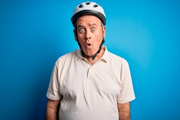 Middle age hoary cyclist man wearing bike security helmet over isolated blue background afraid and shocked with surprise expression, fear and excited face.