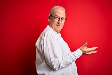 Middle age handsome hoary man wearing casual shirt and glasses over red background pointing aside with hands open palms showing copy space, presenting advertisement smiling excited happy