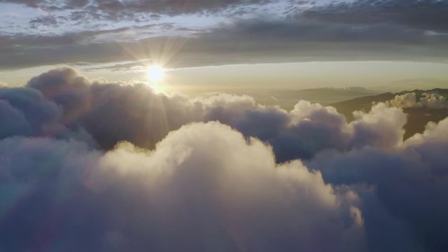 Aerial, tracking, drone shot panning over clouds and the Pacific sea, above mountains in Maui, at sunrise, in Hawaii, USA