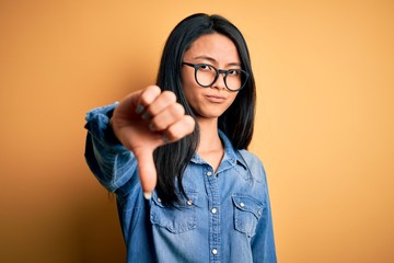 Young beautiful chinese woman wearing casual denim shirt over isolated yellow background looking...