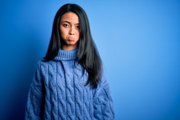 Young beautiful chinese woman wearing casual sweater over isolated blue background depressed and worry for distress, crying angry and afraid. Sad expression.