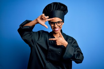 Young african american chef woman wearing cooker uniform and hat over blue background smiling making frame with hands and fingers with happy face. Creativity and photography concept.