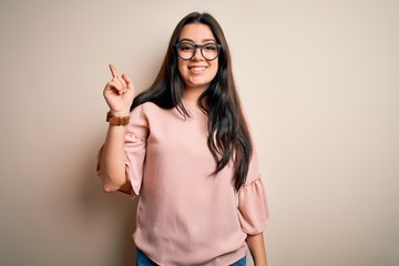 Young brunette elegant woman wearing glasses over isolated background with a big smile on face, pointing with hand and finger to the side looking at the camera.