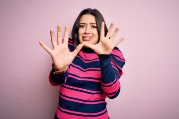 Young brunette elegant woman wearing striped shirt over pink isolated background afraid and terrified with fear expression stop gesture with hands, shouting in shock. Panic concept.