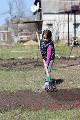 a little white dark-haired white girl with a ponytail outdoors holds a long wooden stick in her hands. Preschooler helps parents in the spring garden