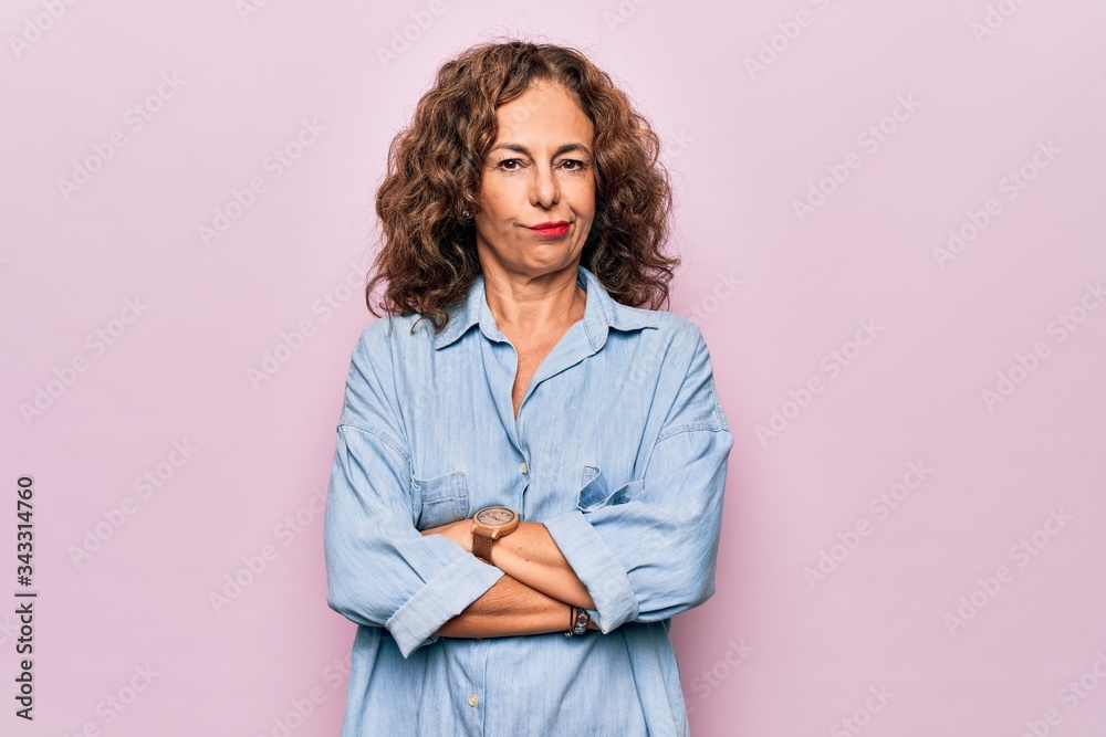 Wall mural middle age beautiful woman wearing casual denim shirt standing over pink background skeptic and nerv