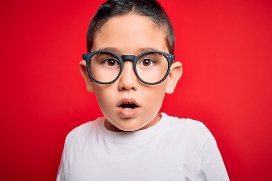 Young little smart boy kid wearing nerd glasses over red isolated background scared in shock with a surprise face, afraid and excited with fear expression