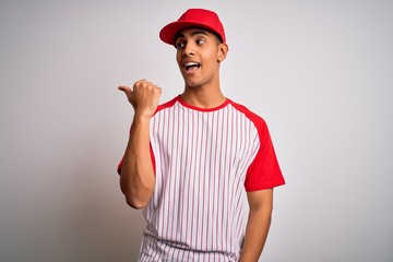 Young handsome african american sportsman wearing striped baseball t-shirt and cap smiling with happy face looking and pointing to the side with thumb up.