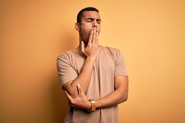 Young handsome african american man wearing casual t-shirt standing over yellow background bored yawning tired covering mouth with hand. Restless and sleepiness.