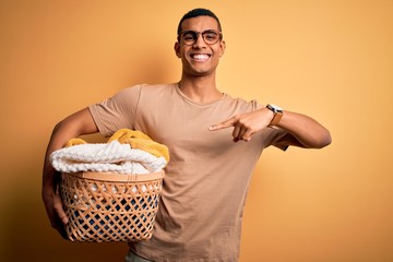 Young handsome african american man doing housework holding wicker basket with clothes very happy pointing with hand and finger