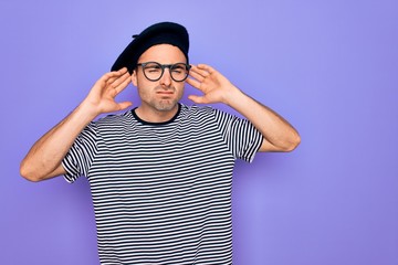 Naklejka premium Handsome man with blue eyes wearing striped t-shirt and french beret over purple background Trying to hear both hands on ear gesture, curious for gossip. Hearing problem, deaf